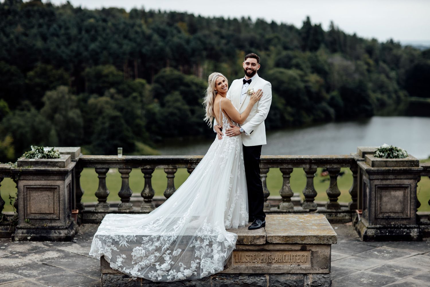 A romantic wedding photo shoot at a grand stone balcony overlooking a scenic lake.