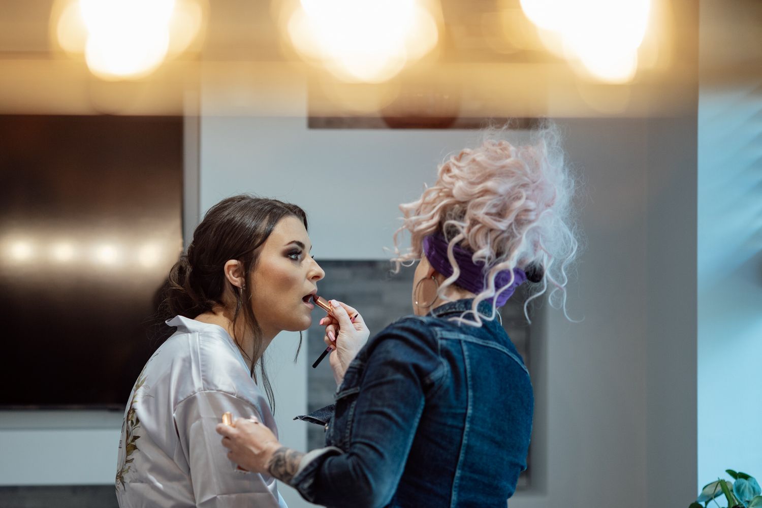 Makeup artist applying cosmetics to a client with purple hair in a professional setting.