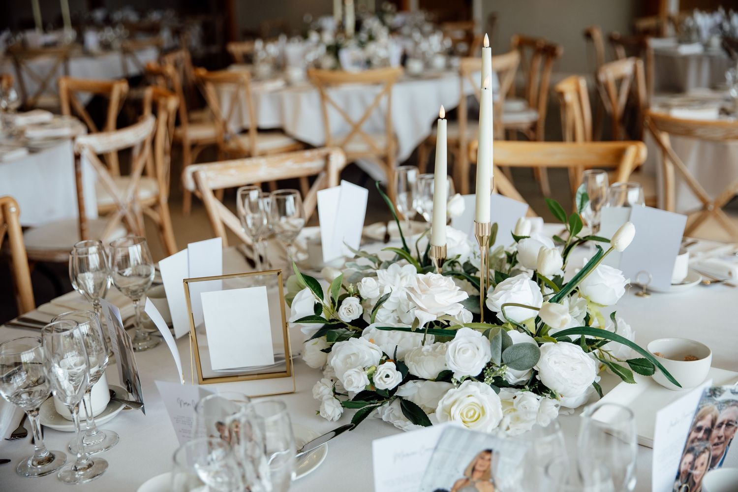 Wedding reception tables set with white floral arrangements, candles and gold accents.