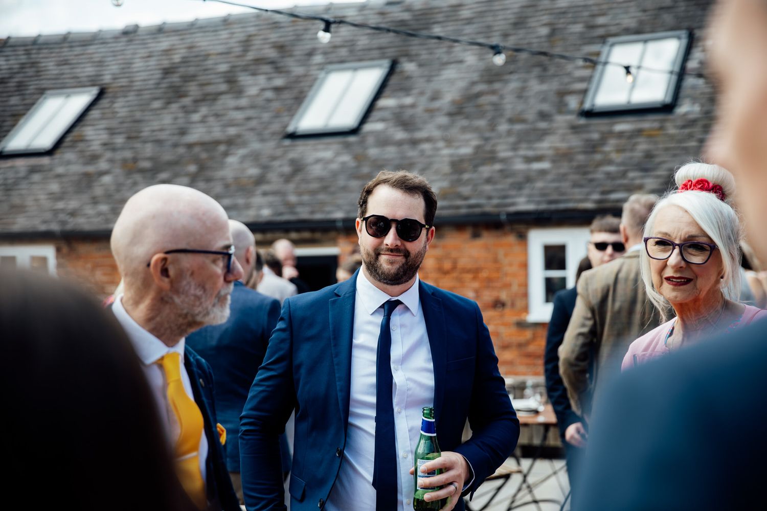 Wedding guests mingle outdoors at a rustic brick venue during a daytime celebration.