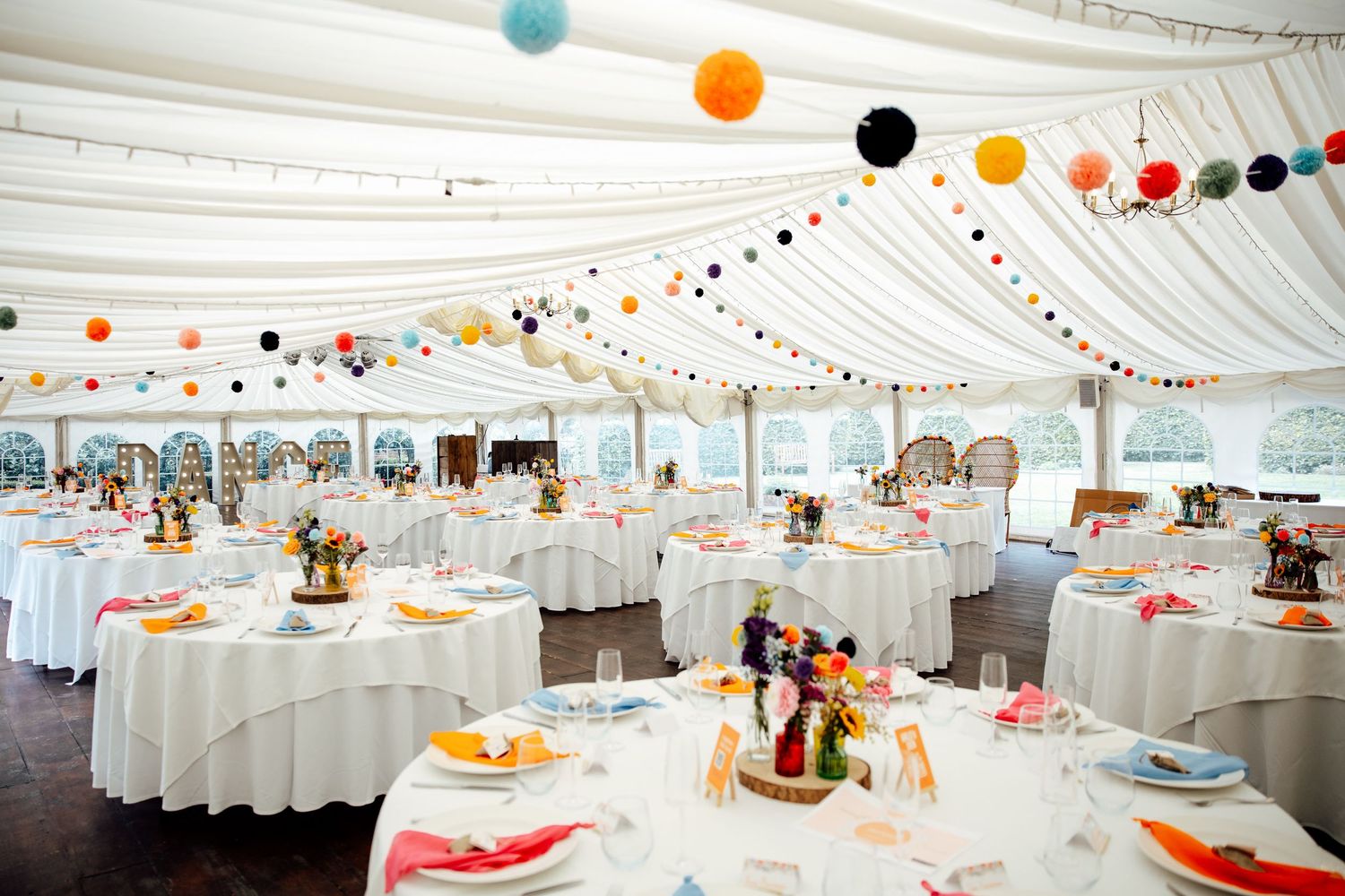 Wedding reception venue decorated with colorful paper lanterns and white tablecloths in an elegant marquee setting.