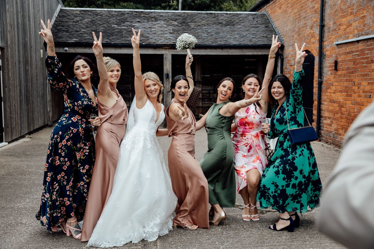 Wedding party poses for group photos against rustic brick wall backdrop.