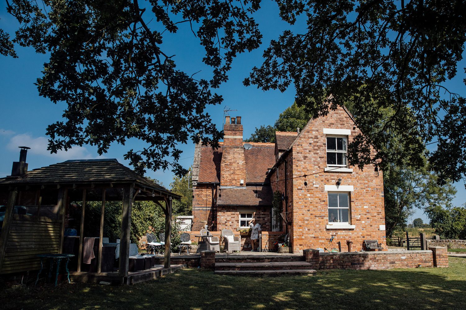Historic brick building serves as backdrop for outdoor wedding venue under blue skies and mature trees.