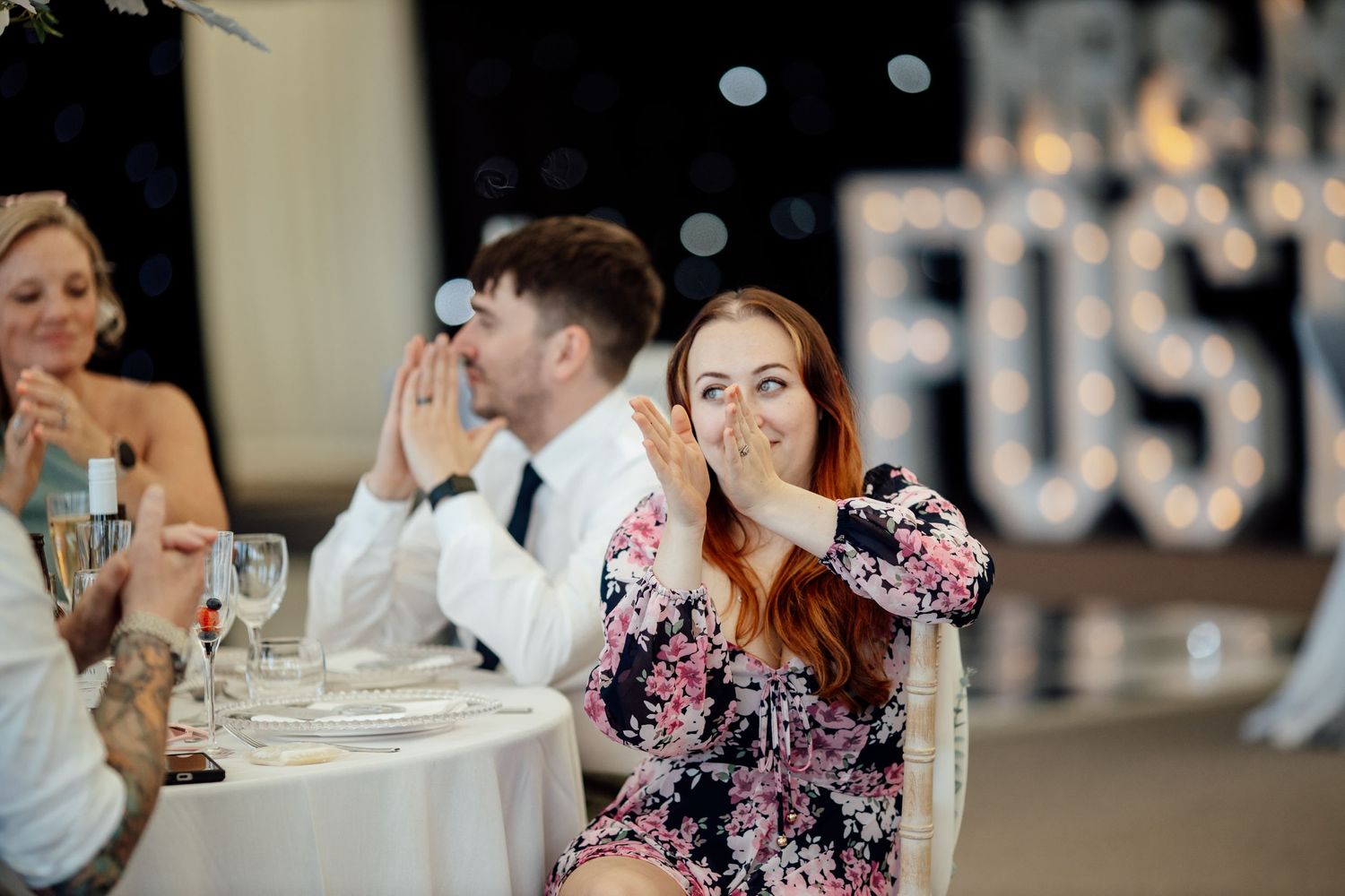 Wedding reception guests enjoying dinner and toasts at decorated indoor tables.