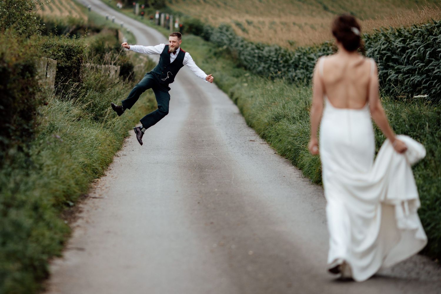Couple walking down country path holding hands with wedding dress trailing behind.