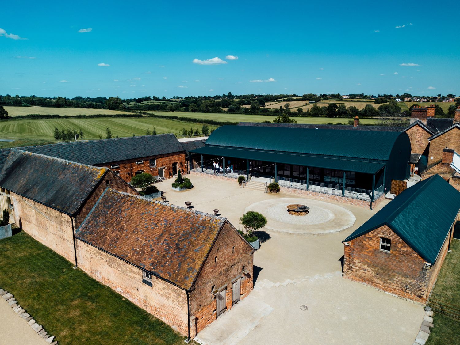 Aerial view of a rustic barn wedding venue with red brick buildings and white gravel courtyard.