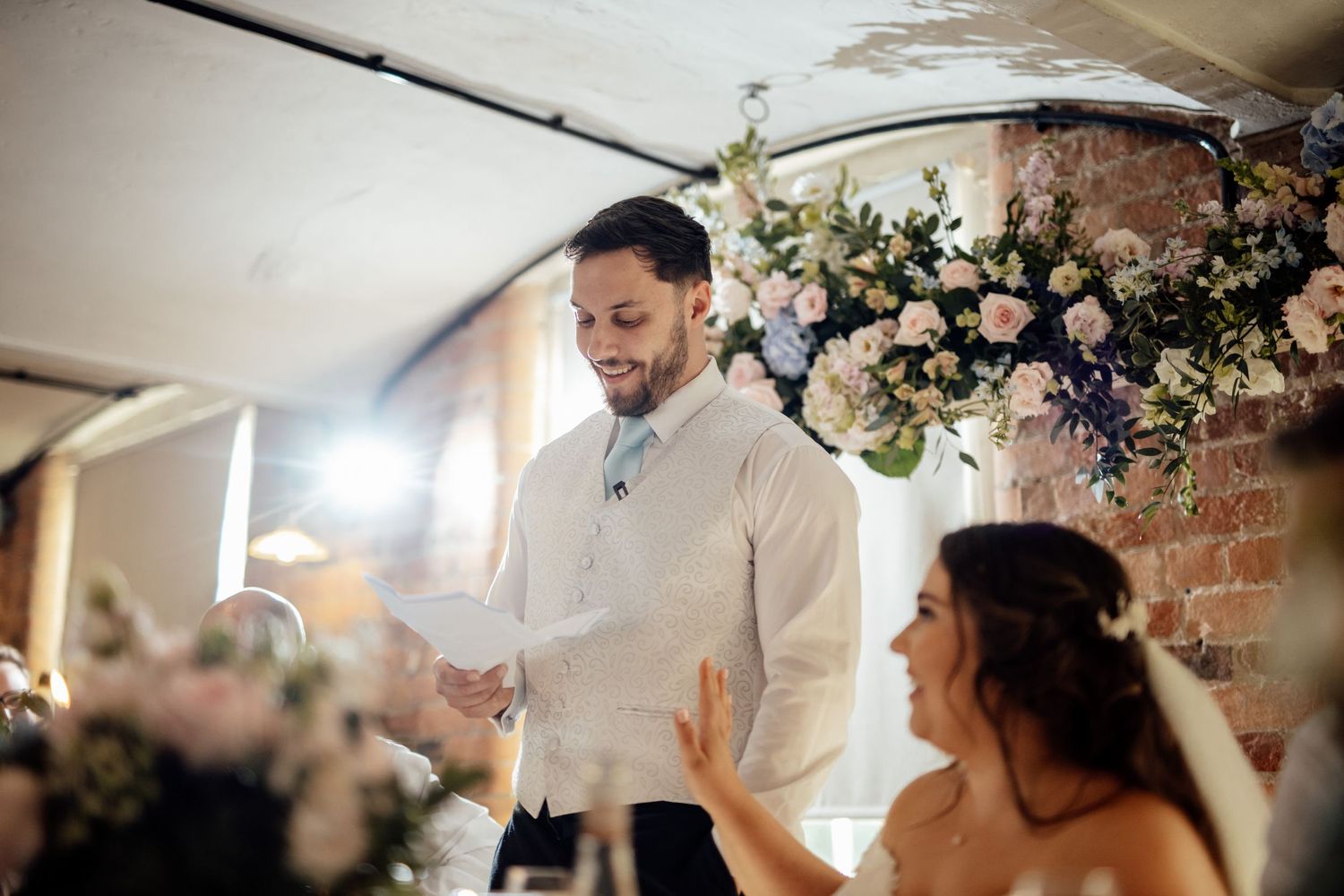 Reception scene with floral arrangements and guests at wedding celebration.