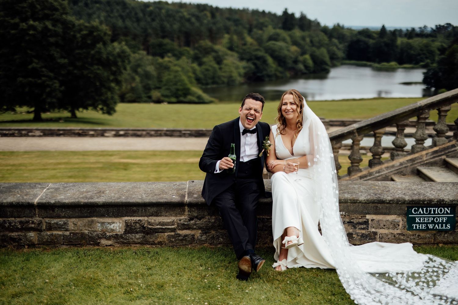Wedding couple posing on stone steps with scenic lake and forest landscape behind them.