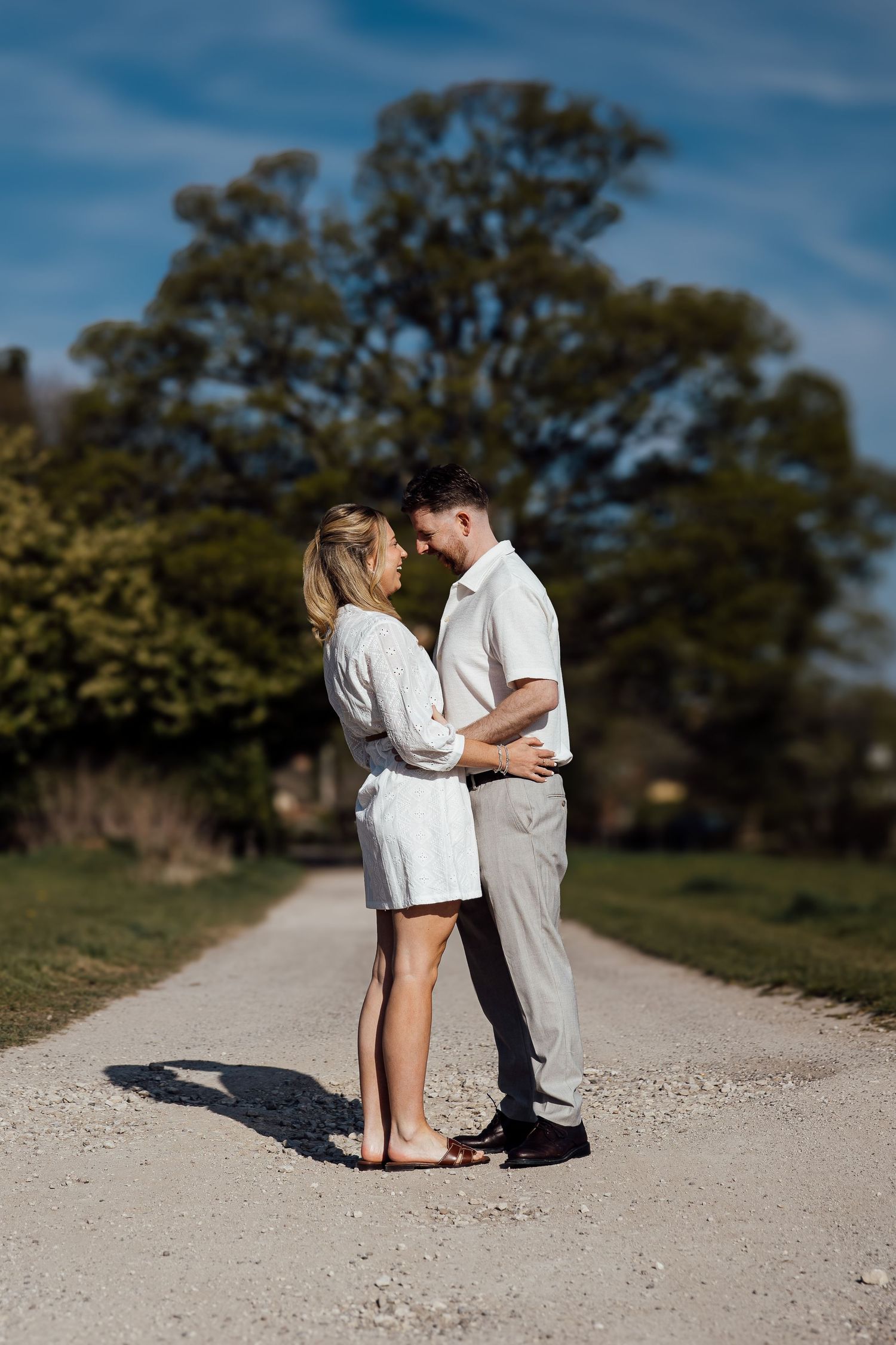 A couple in light-colored outfits sharing an intimate moment on a gravel path.