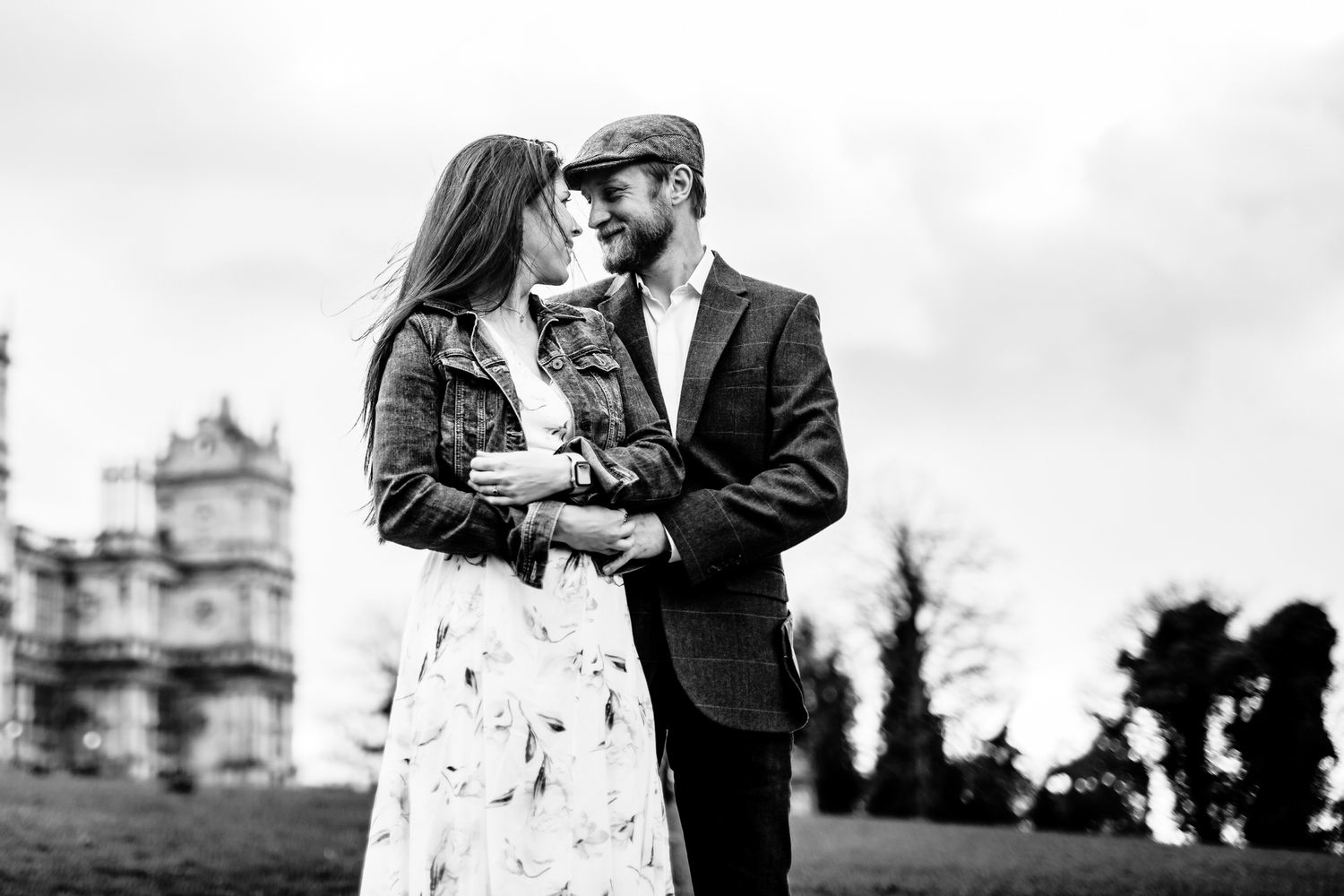 Romantic couple embraces on a path with historic architecture visible in the background.