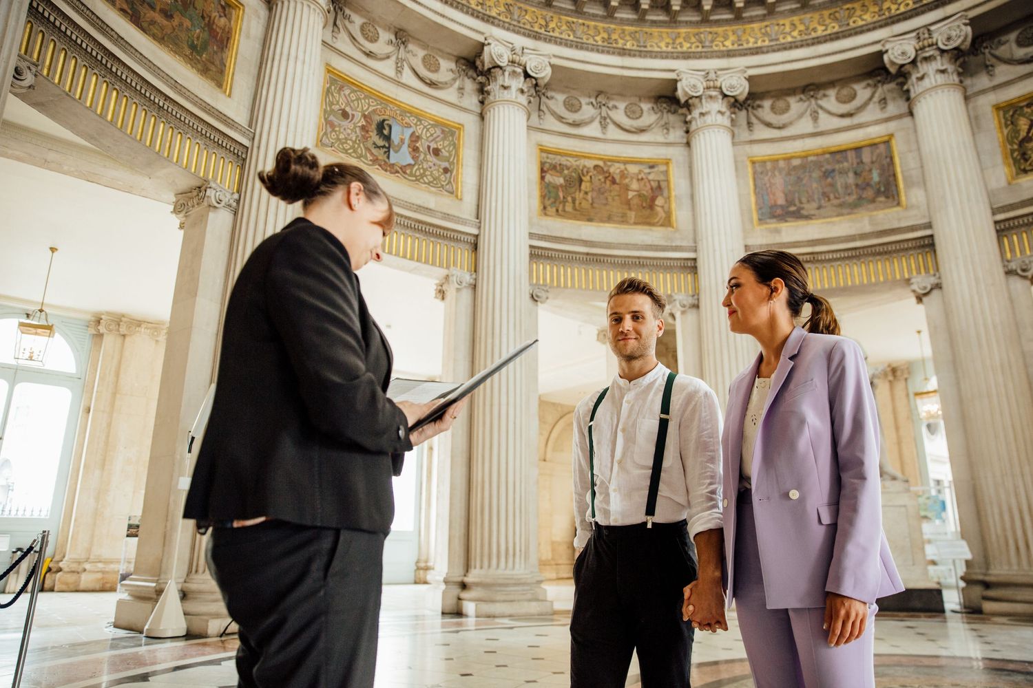 People gather in a historic building interior featuring white columns and ornate domed ceiling.