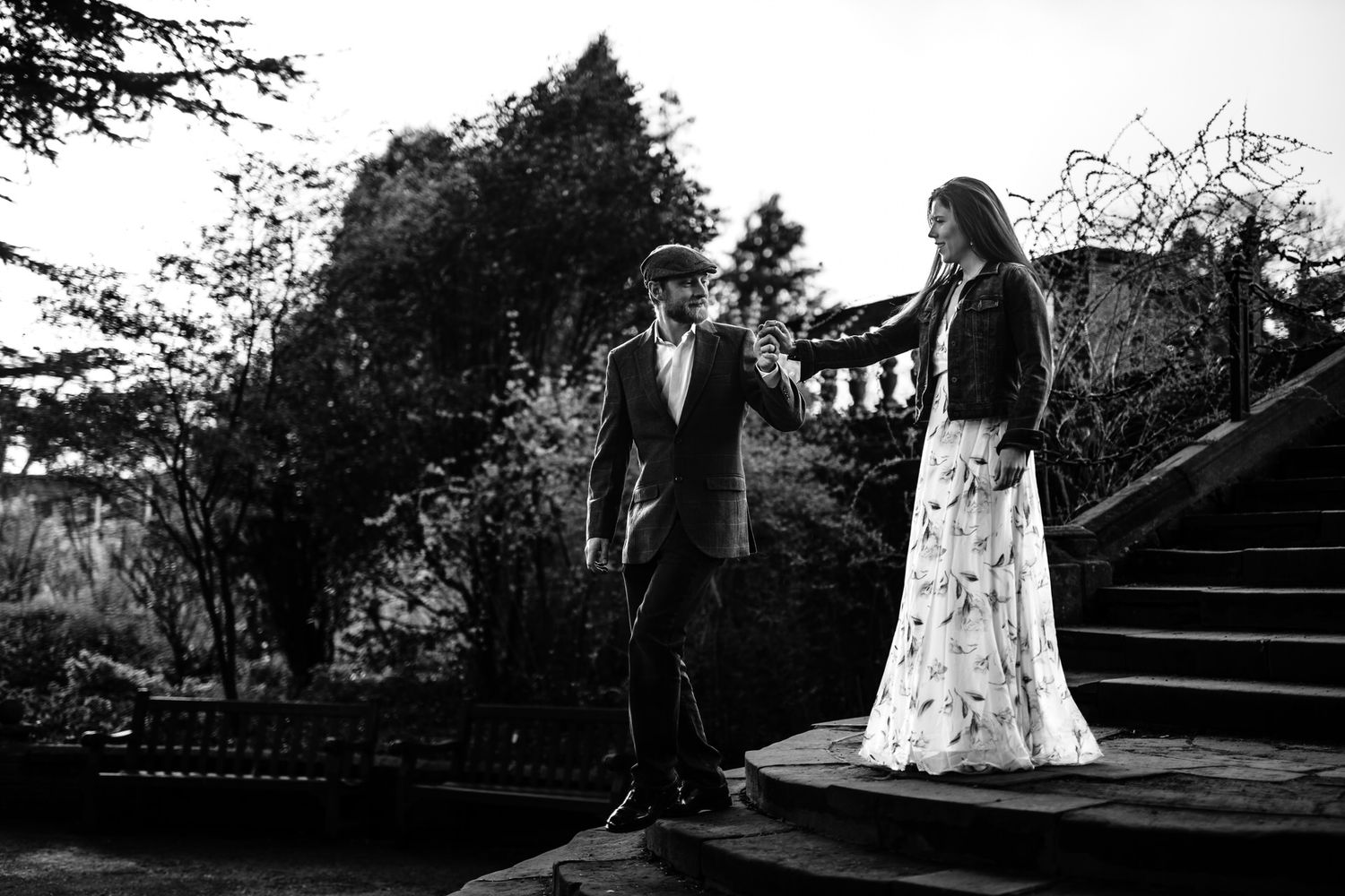 A black and white portrait of a couple on outdoor steps surrounded by foliage.