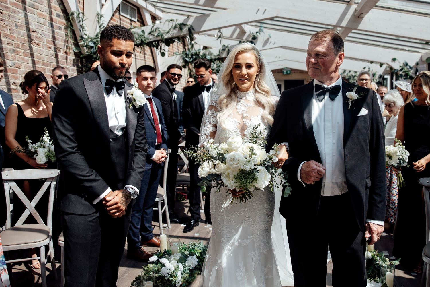 Wedding party walks through an elegant glass-roofed venue during the ceremony.