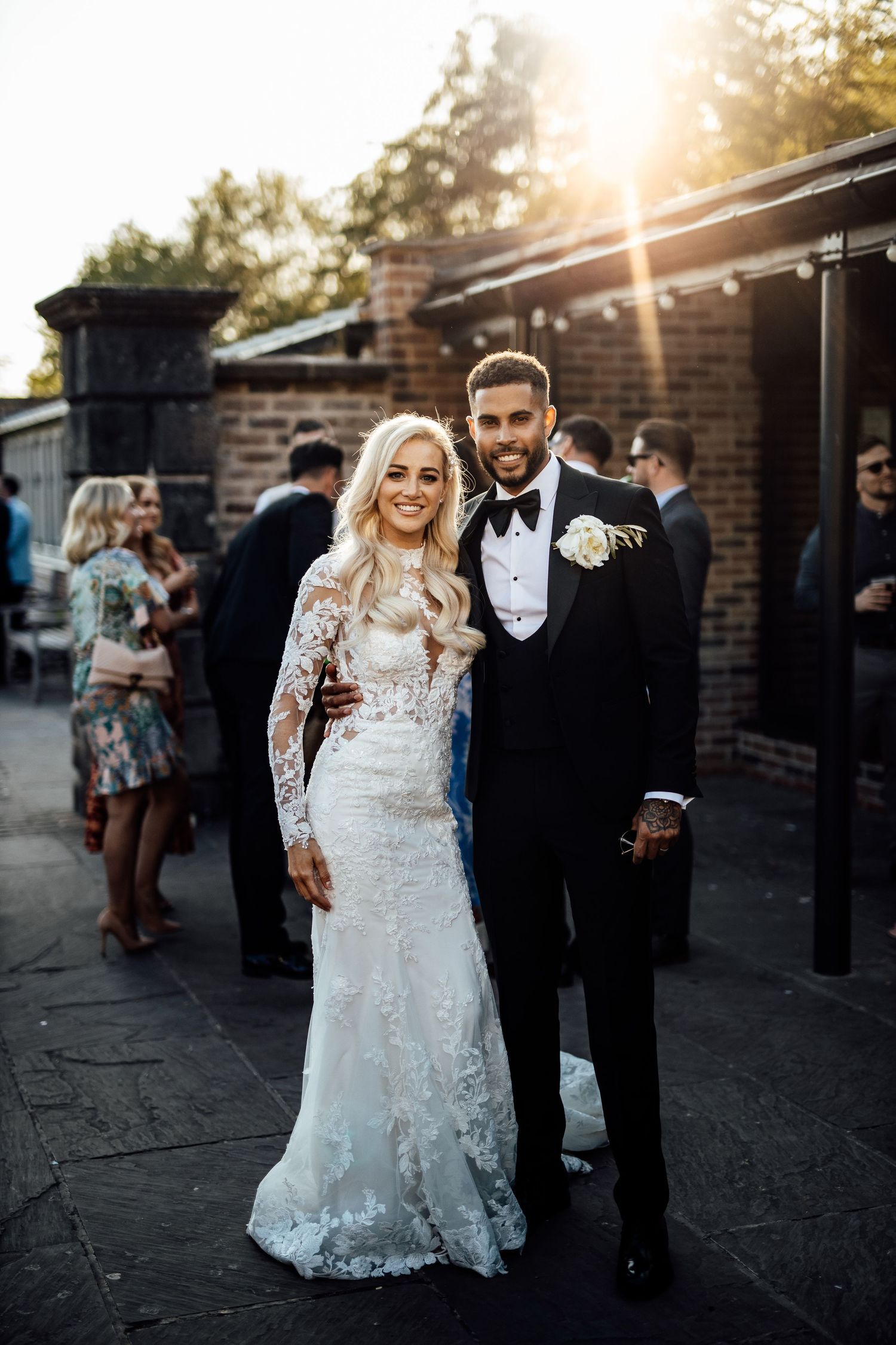 Couple poses for sunset portraits outside a brick venue in formal wedding attire.