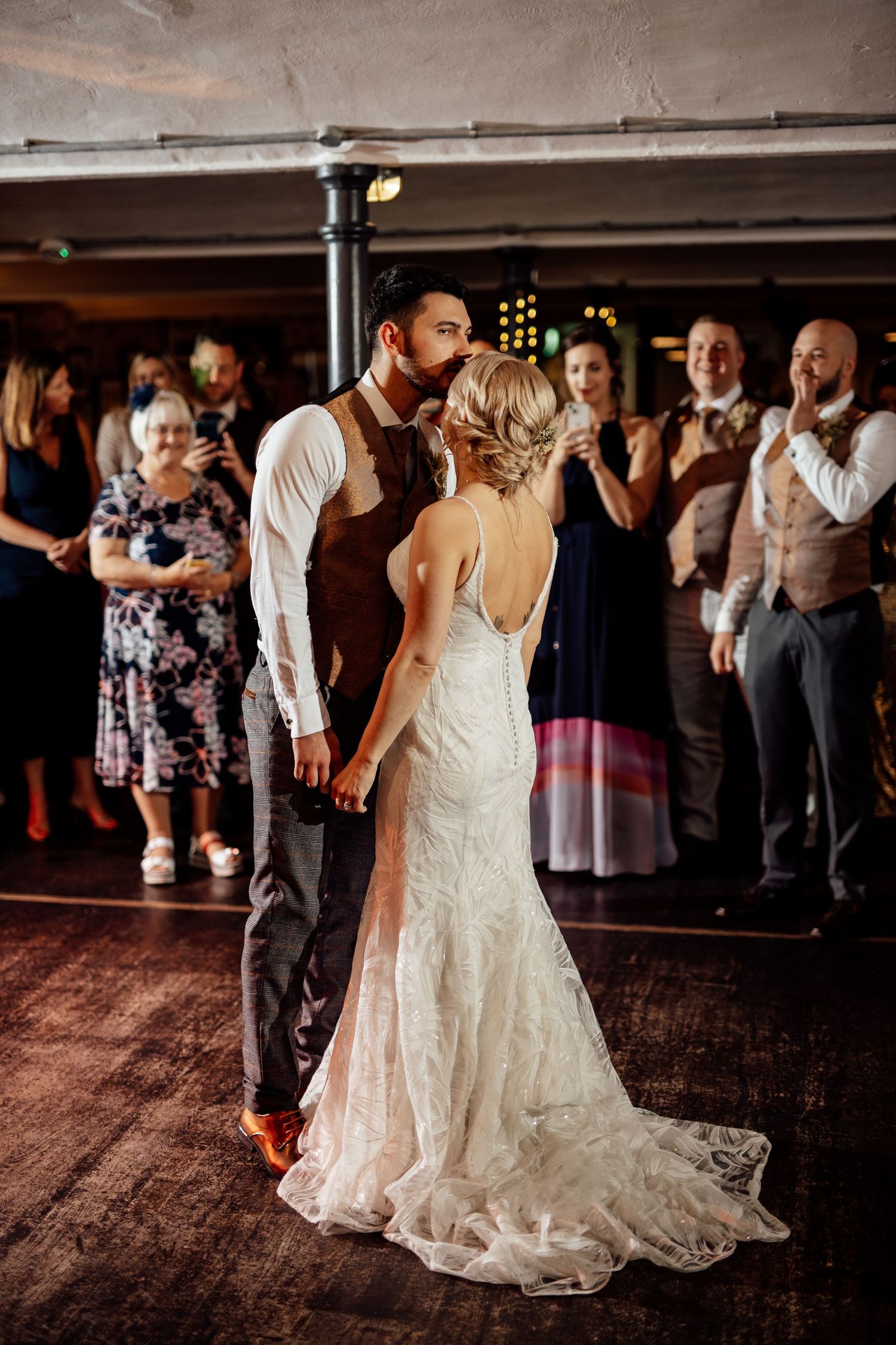 Wedding celebration on a dark wooden dance floor with guests dancing in formal attire.