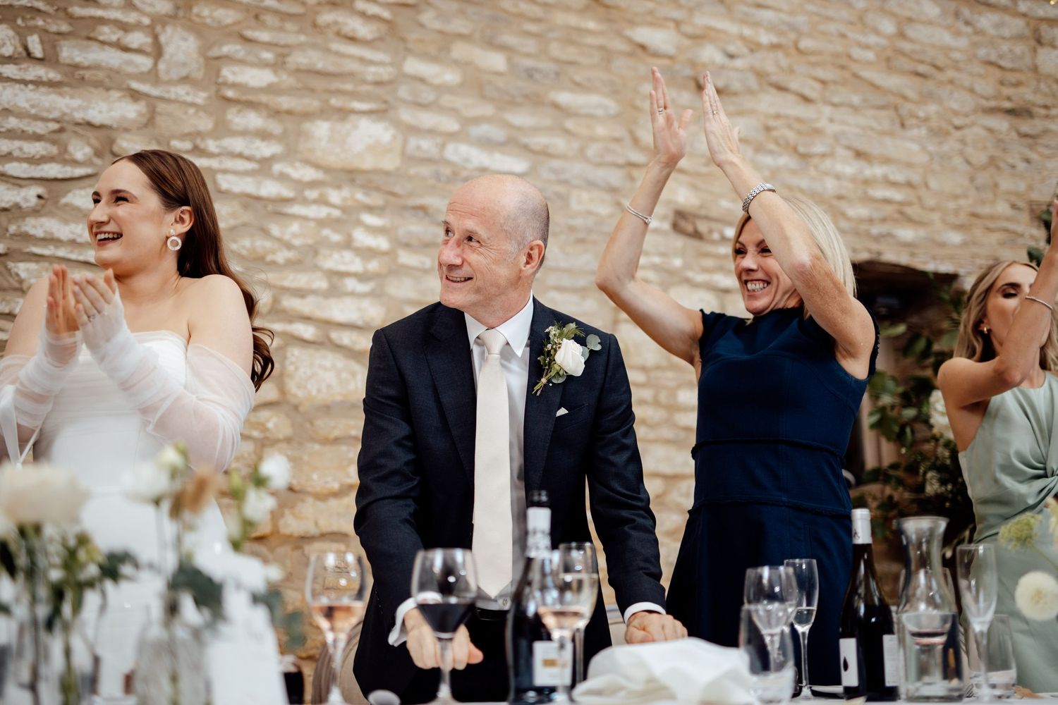 Wedding guests enjoying dinner and toasts at reception tables.