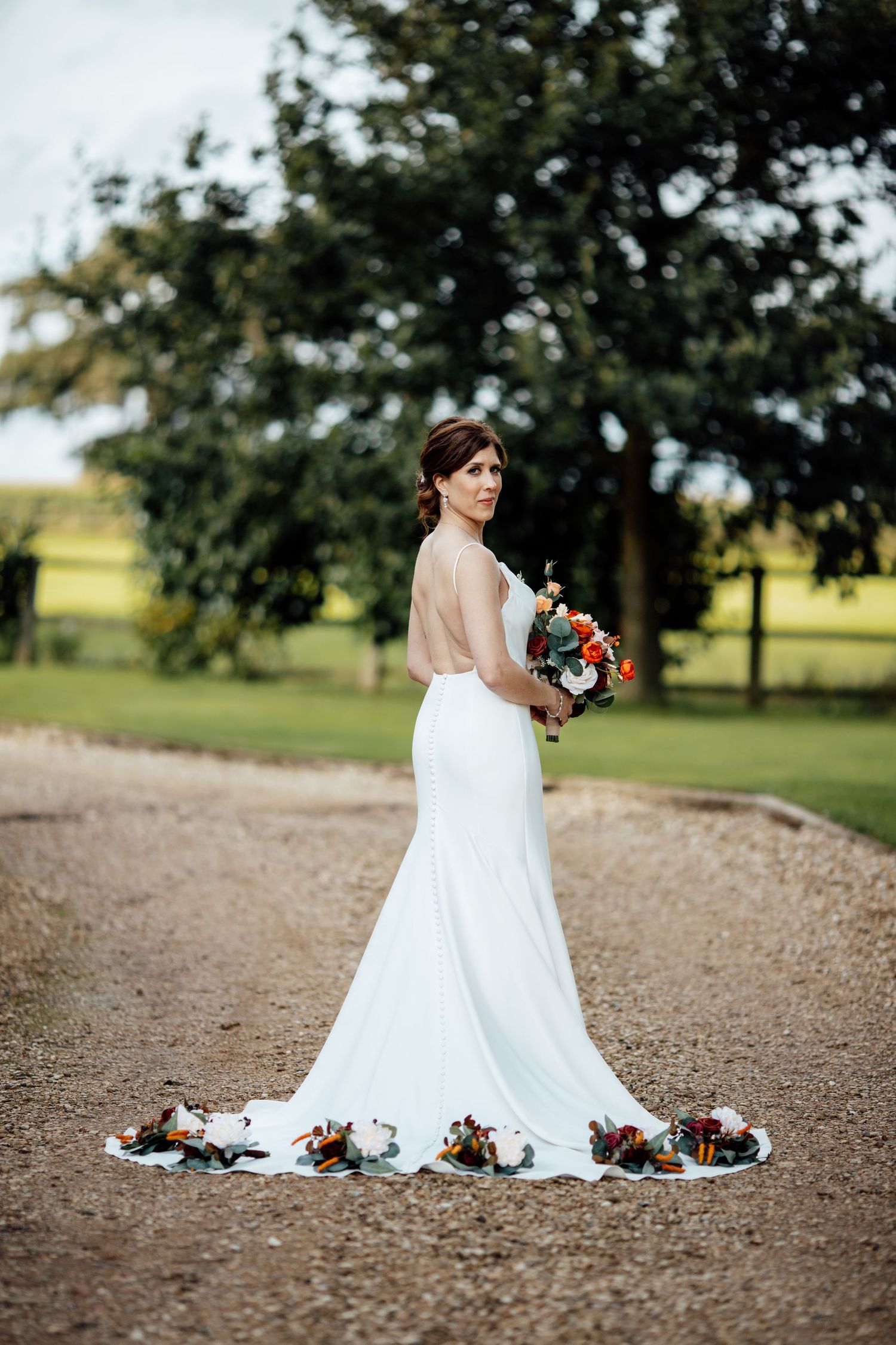 White wedding dress trailing on a gravel path with trees in the background.