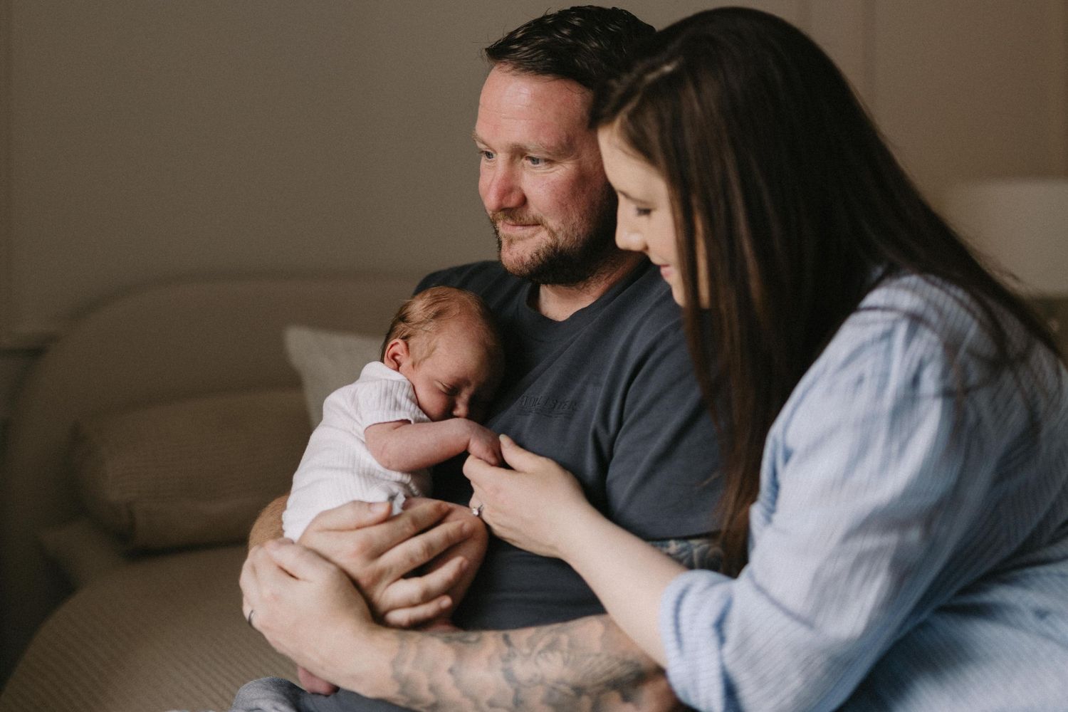 New parents tenderly cradling their sleeping newborn baby together, sharing a precious family moment at home.