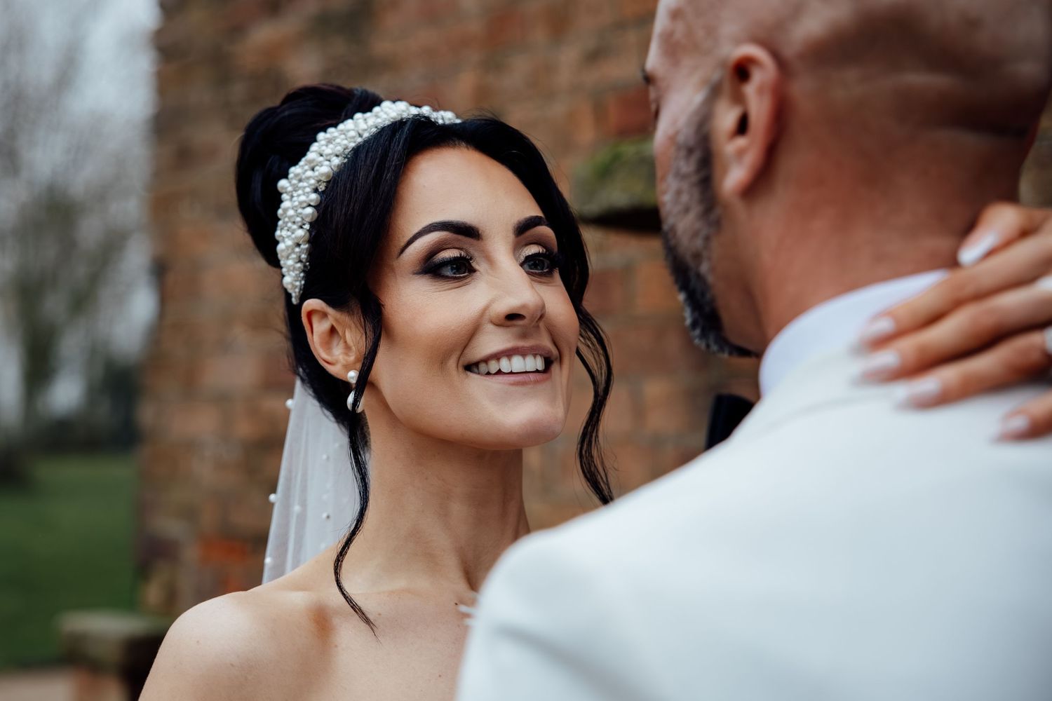 Elegant wedding couple sharing intimate moment outdoors near brick wall.