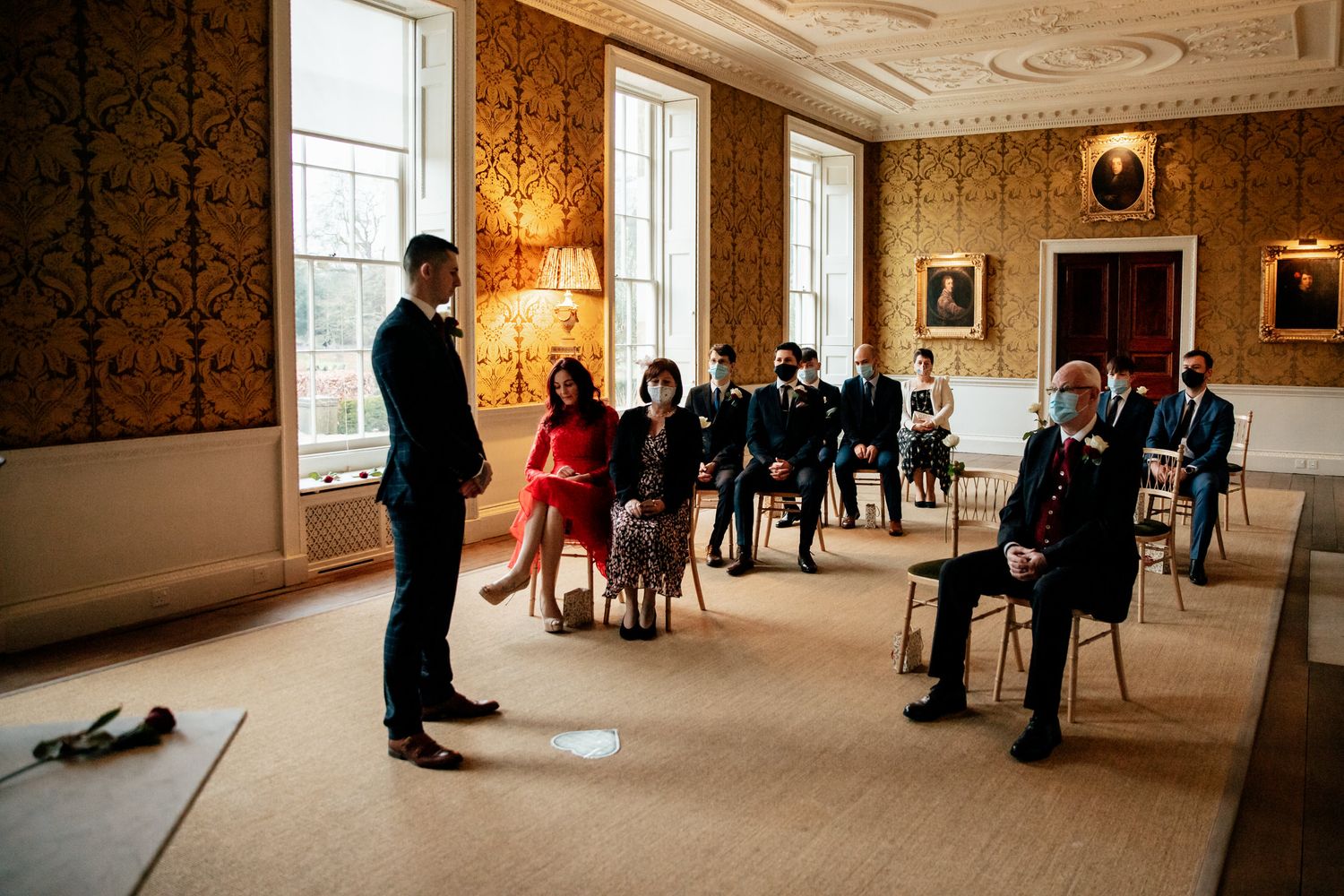 Wedding ceremony in an ornate room with damask wallpaper and classic portraits.