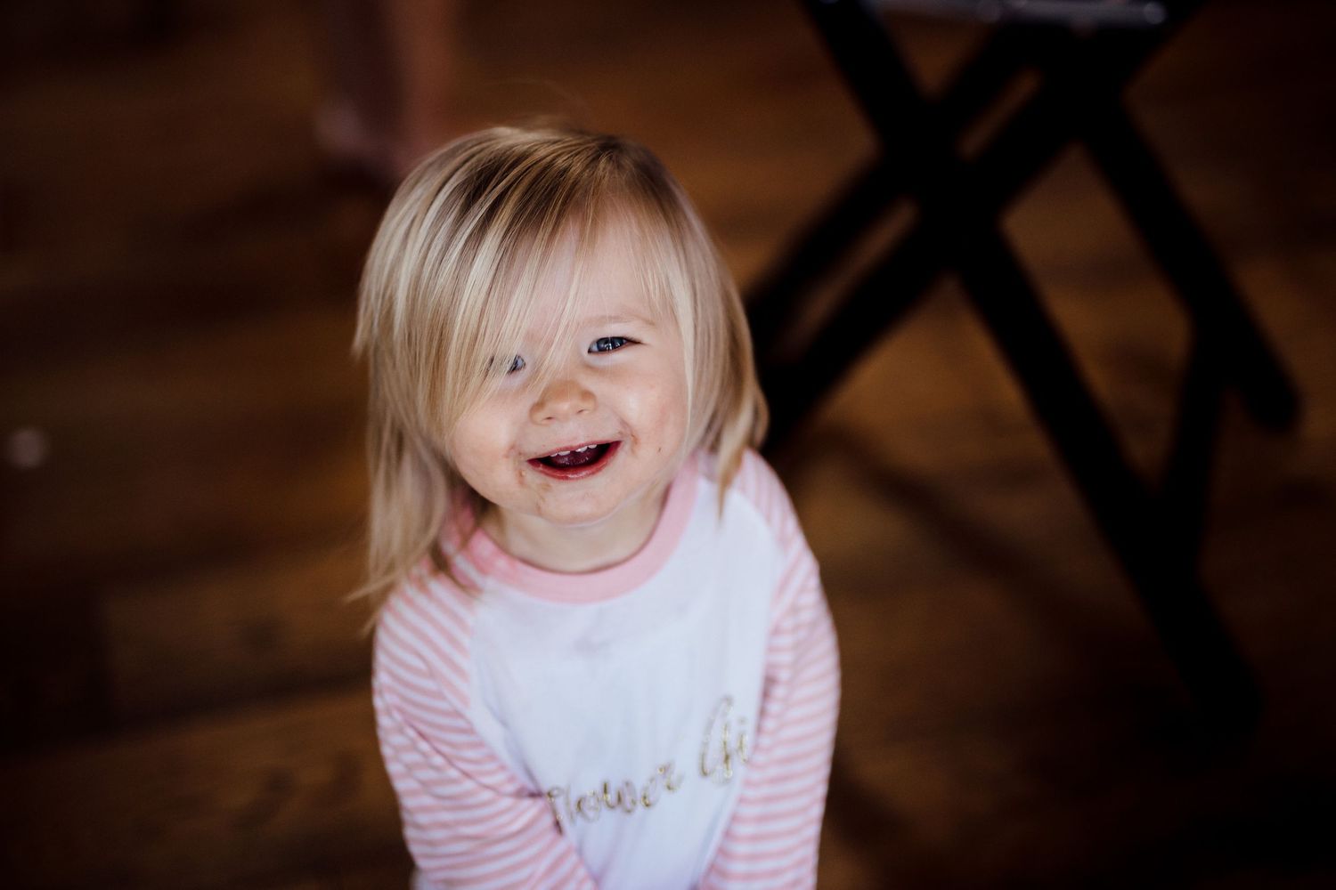A young child in pink smiling and laughing in warm indoor lighting.