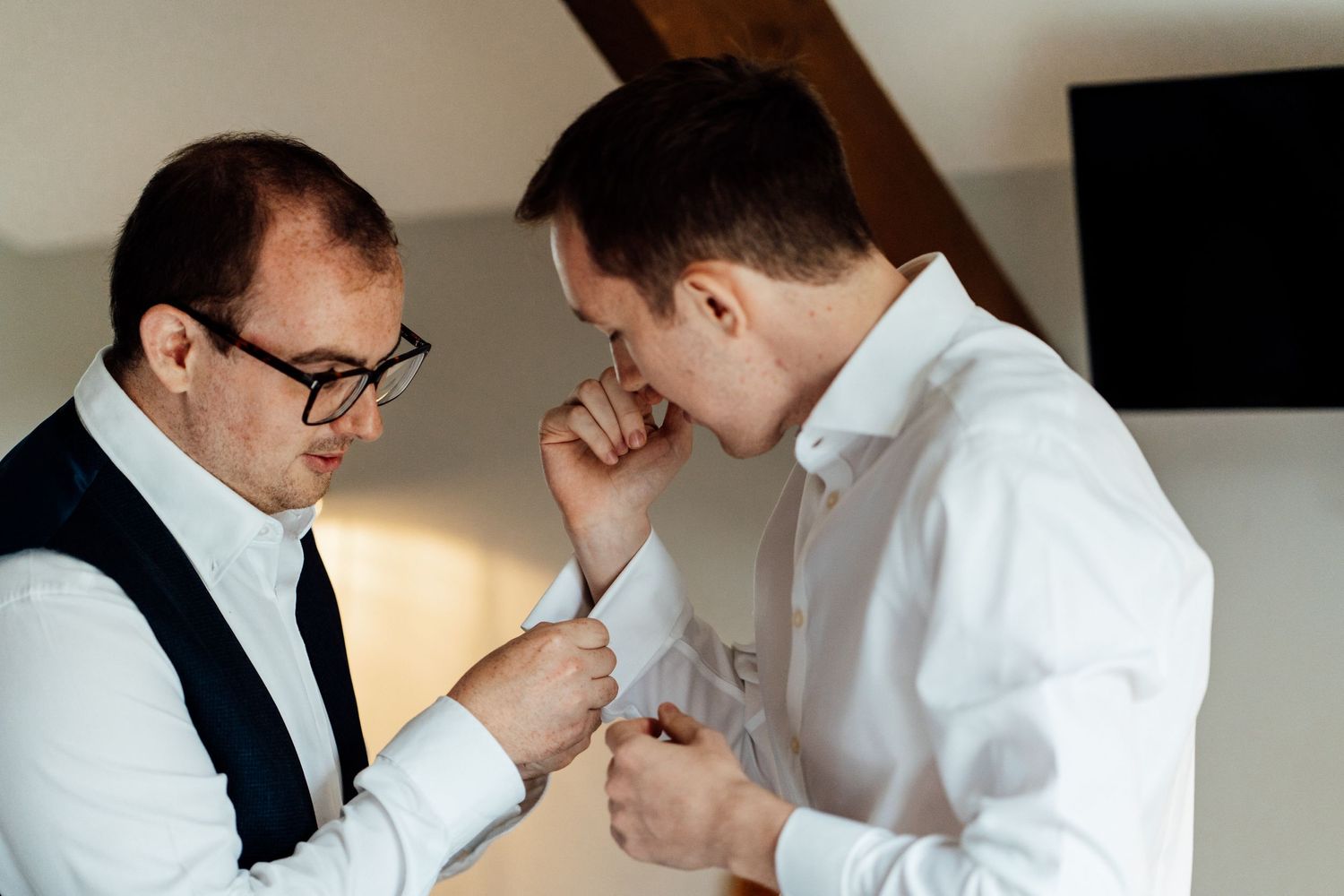 Groomsmen helping with wedding day preparations in bright room.