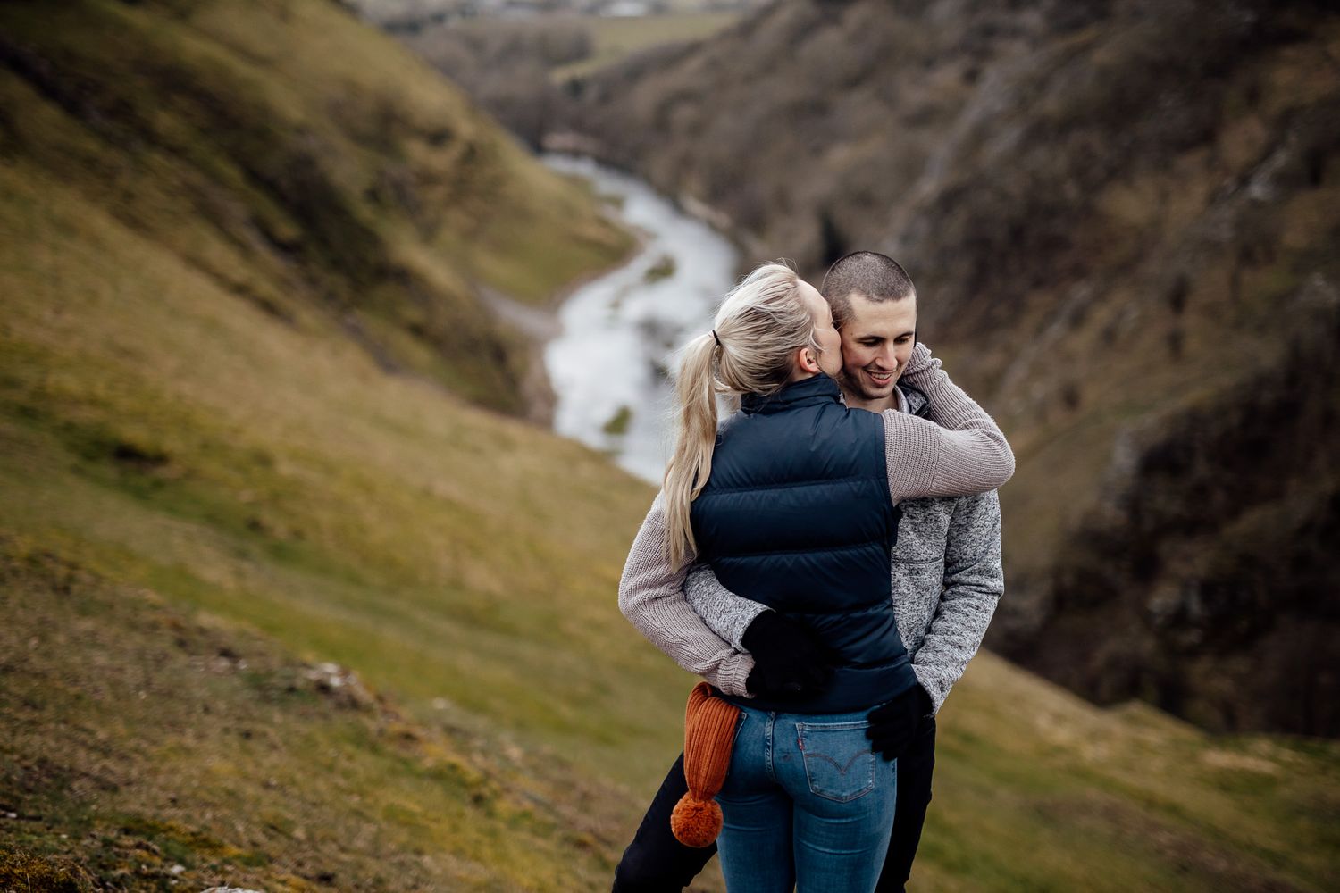 A couple shares an intimate moment against a dramatic mountain landscape backdrop.