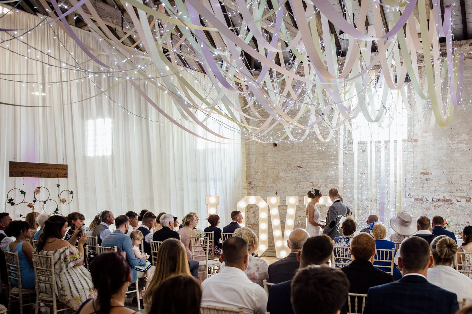 Wedding reception hall decorated with elegant white draping and hanging decorations.