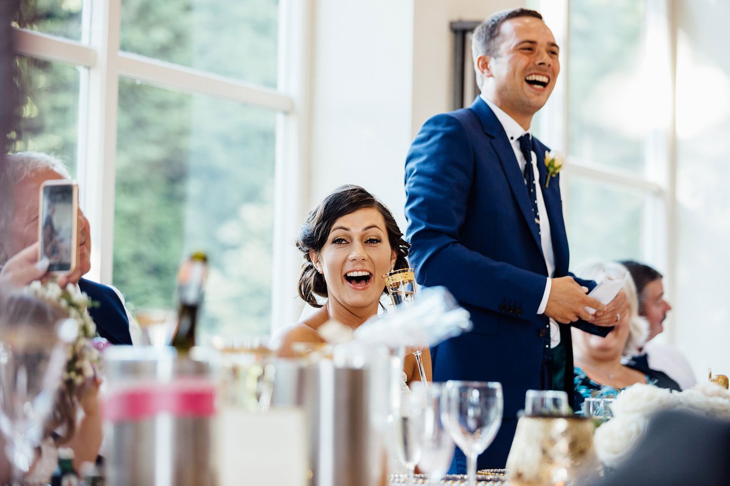 Wedding guests laugh and celebrate during a joyful reception moment.
