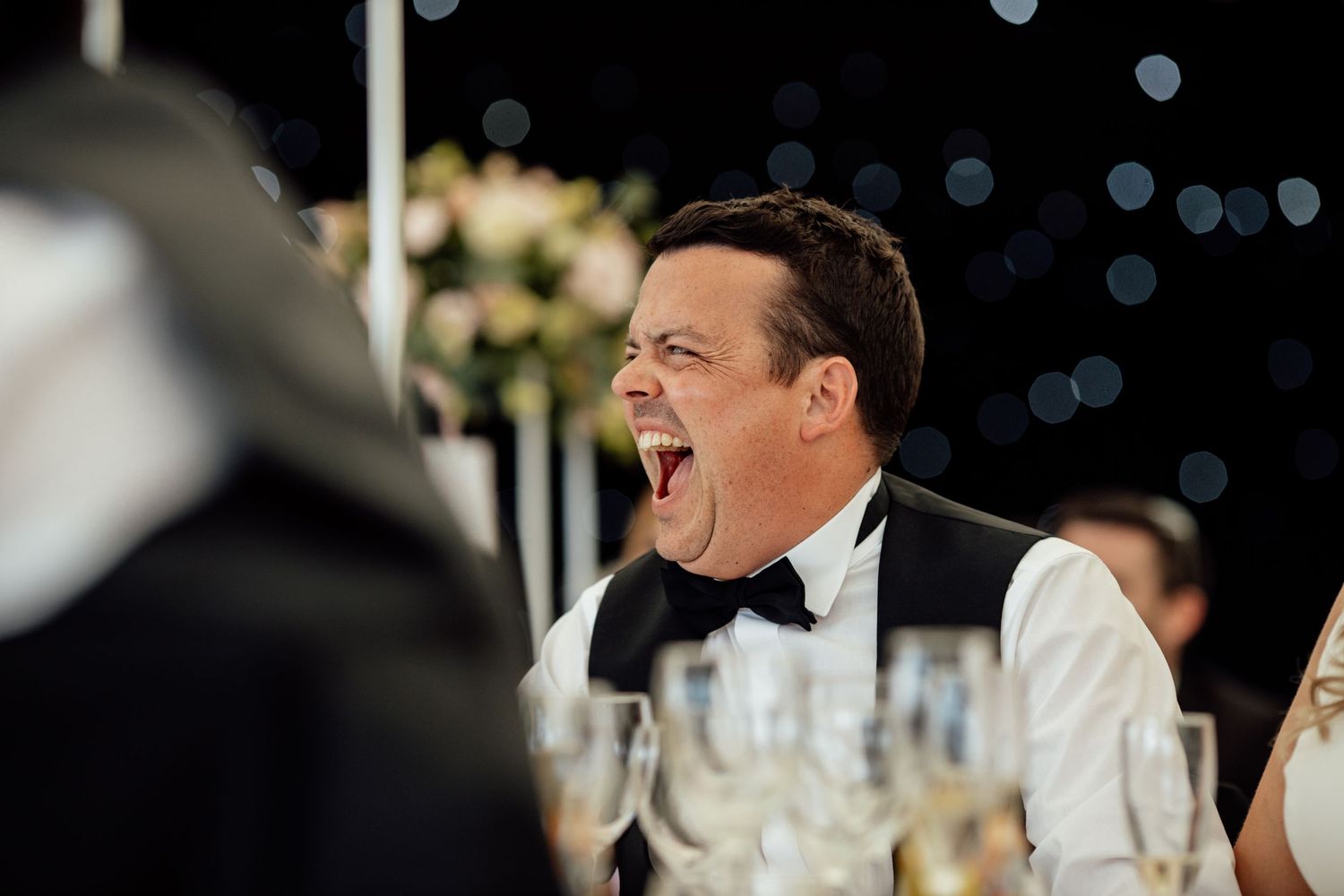 Wedding reception guests laughing during evening dinner celebrations.
