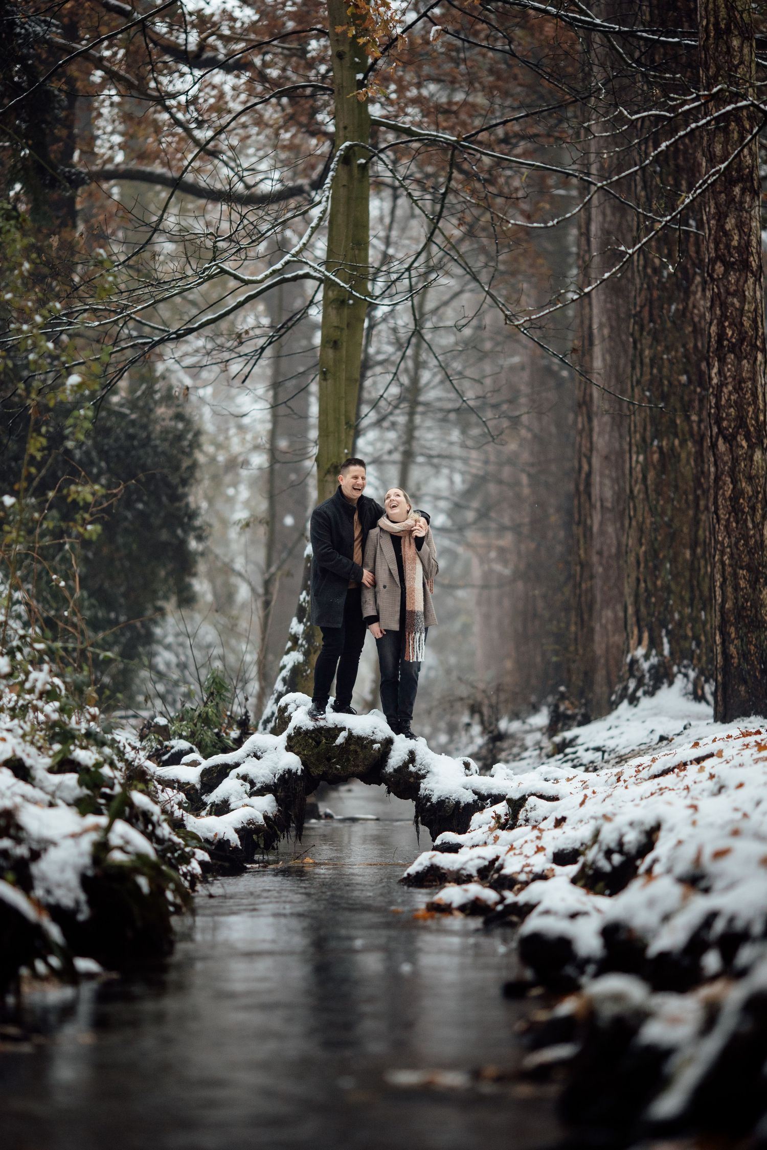 A winter engagement photo in a forest with snow-lined path and bare trees.