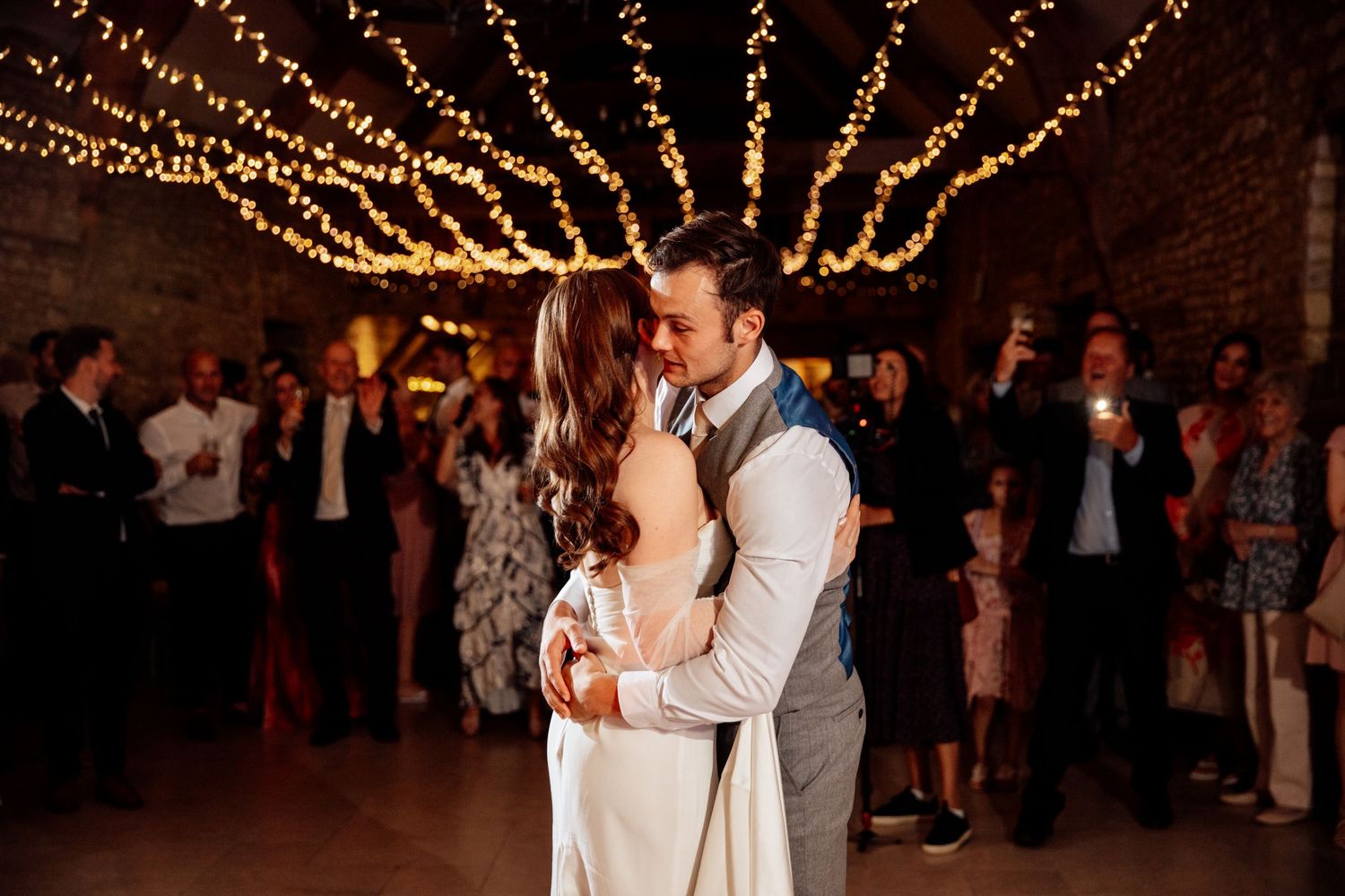 Newlyweds share their first dance under warm string lights at their reception.