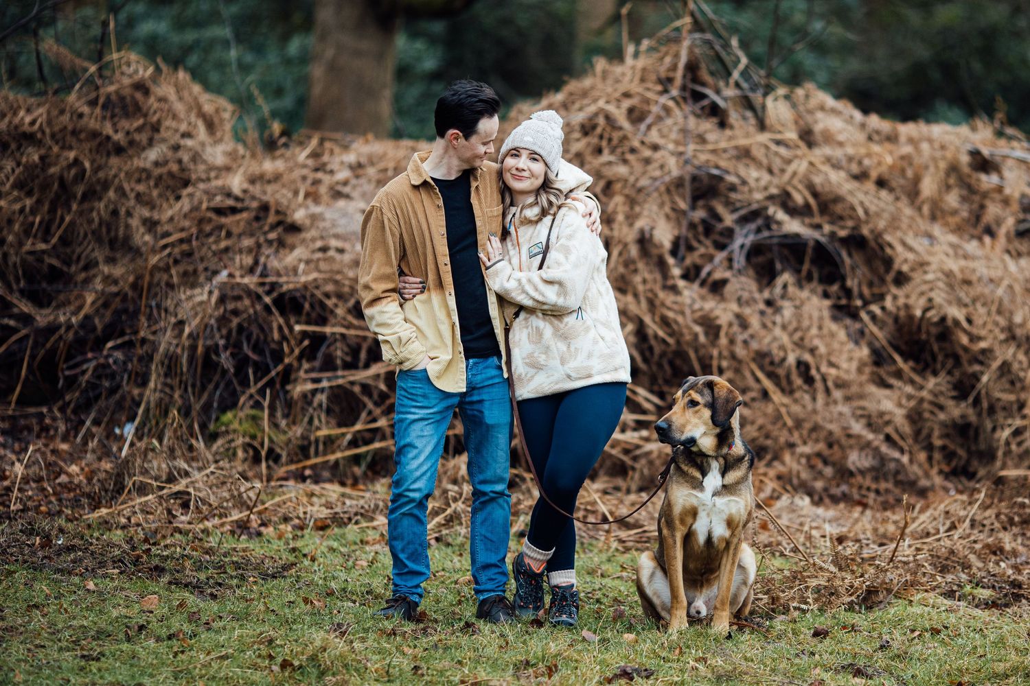 Couple enjoying a walk with their dog on a nature trail surrounded by autumn foliage.