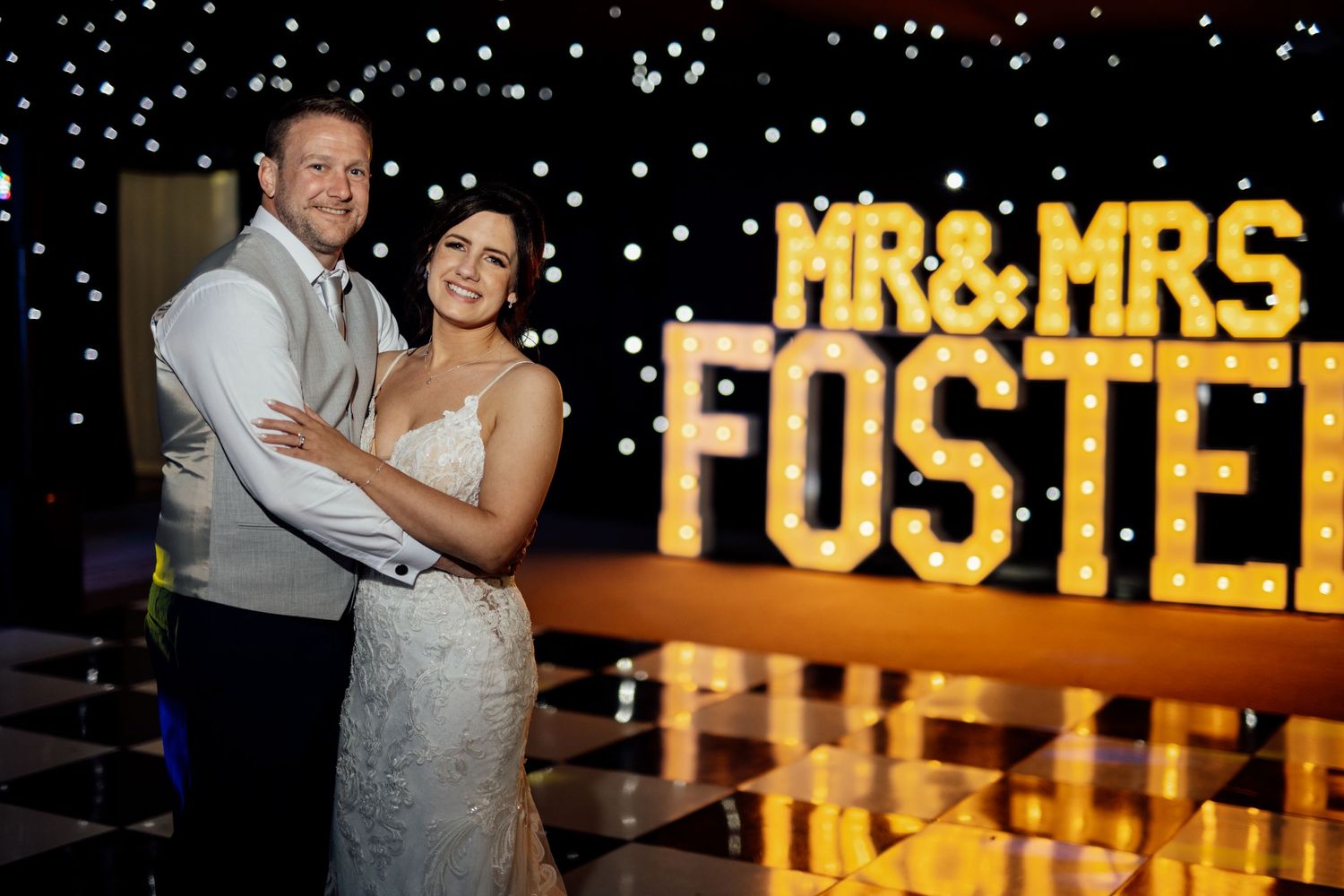 Illuminated 'Mr & Mrs' sign glows warmly at evening wedding reception.