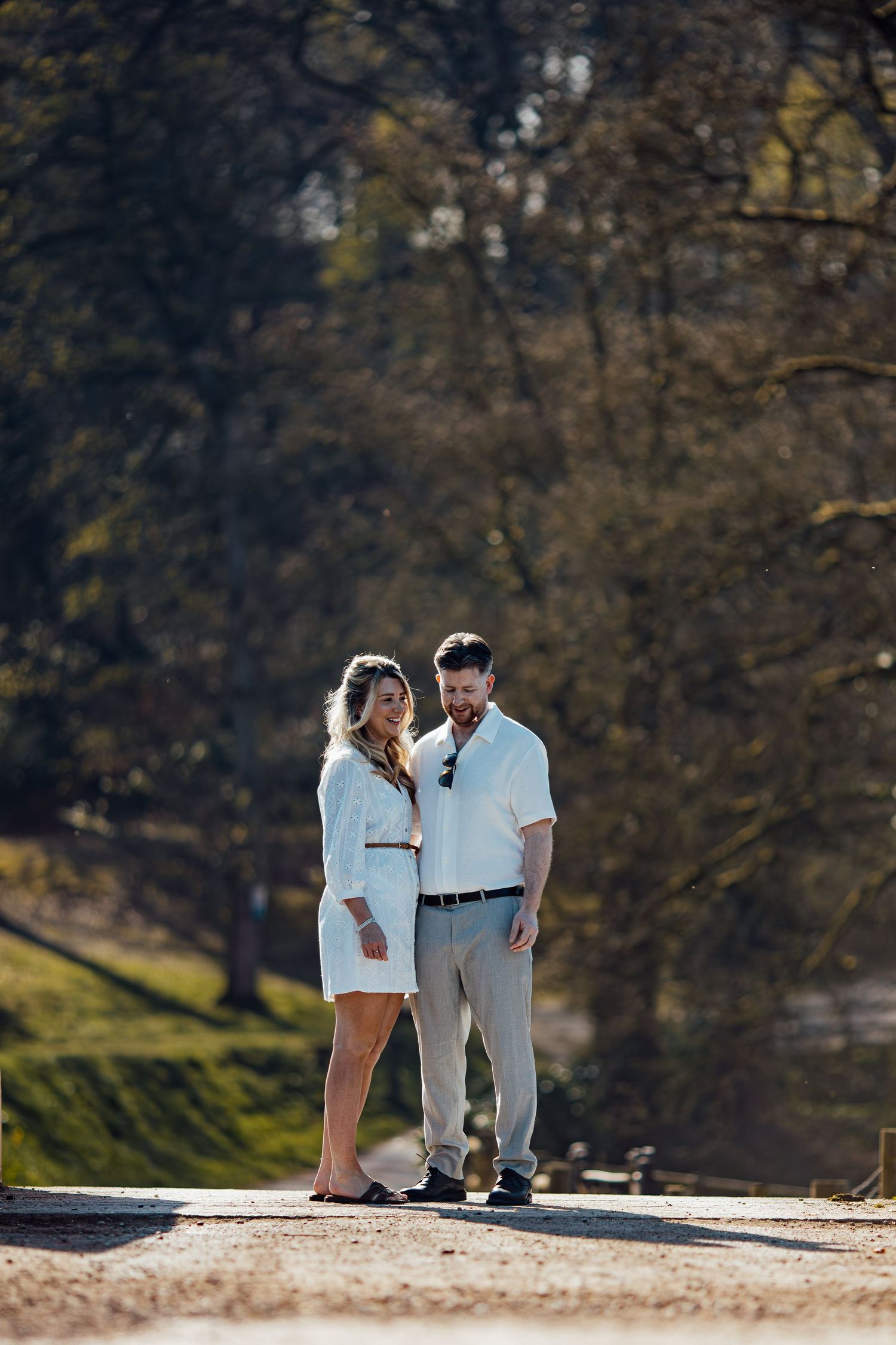 A couple dressed in white enjoys a tender moment on a path surrounded by autumn trees.