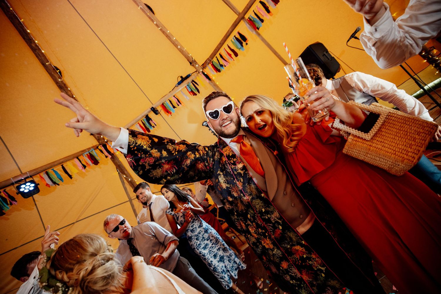 Wedding reception dance party under warm lighting with guests celebrating.