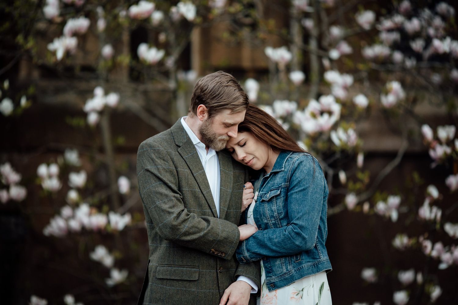 Intimate moment between couple with blooming magnolia trees in background.
