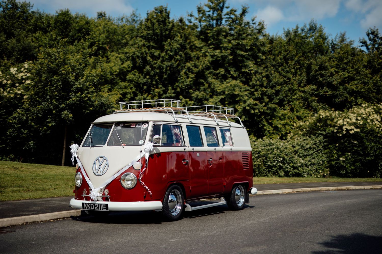 A classic red and white Volkswagen bus parked on a tree-lined road.