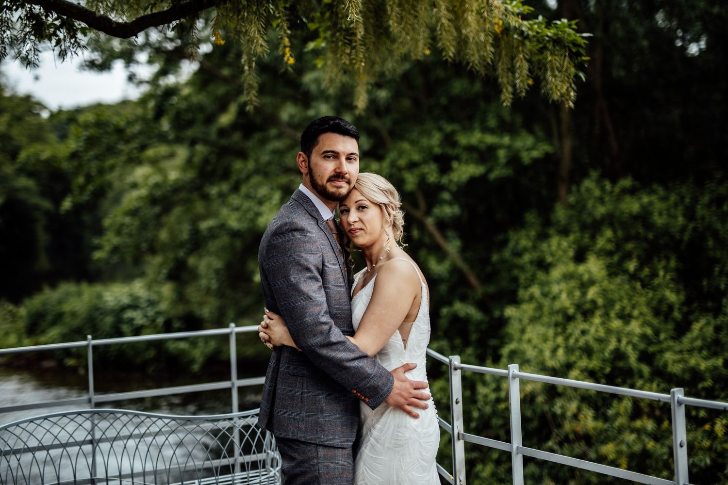 Wedding couple embracing on an outdoor terrace surrounded by lush green trees.