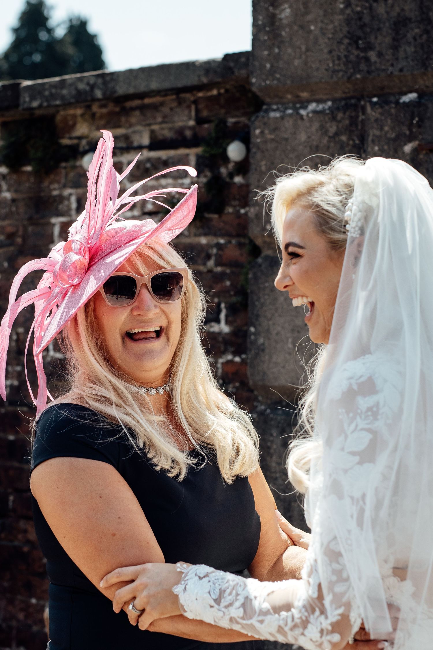 Wedding party members share laughter and hugs against a brick wall backdrop.