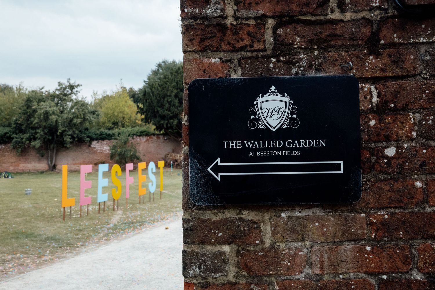 Walled Garden venue sign on brick wall with colorful letters in background.