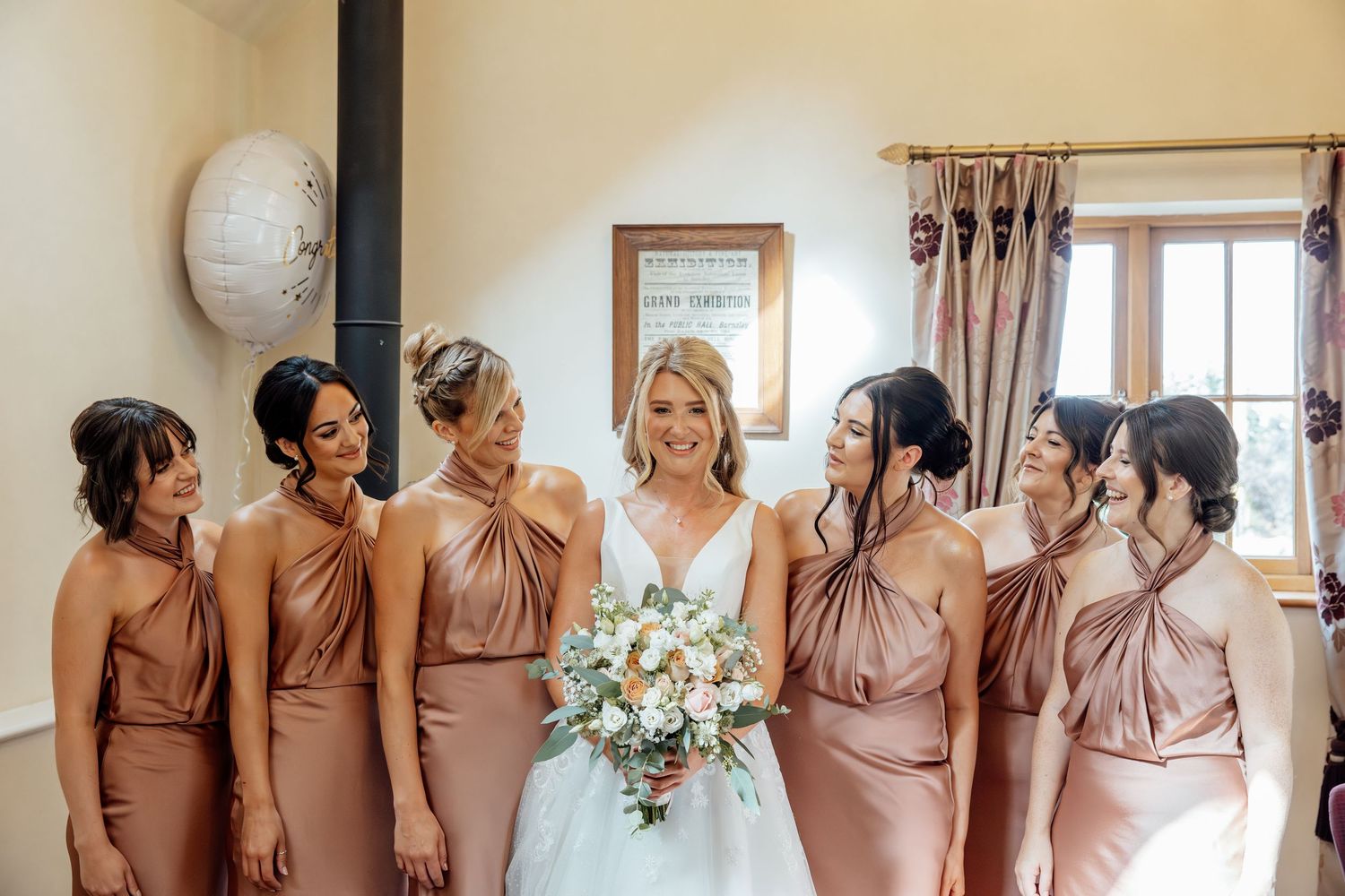 Wedding party wearing matching dusty rose dresses posing together indoors.