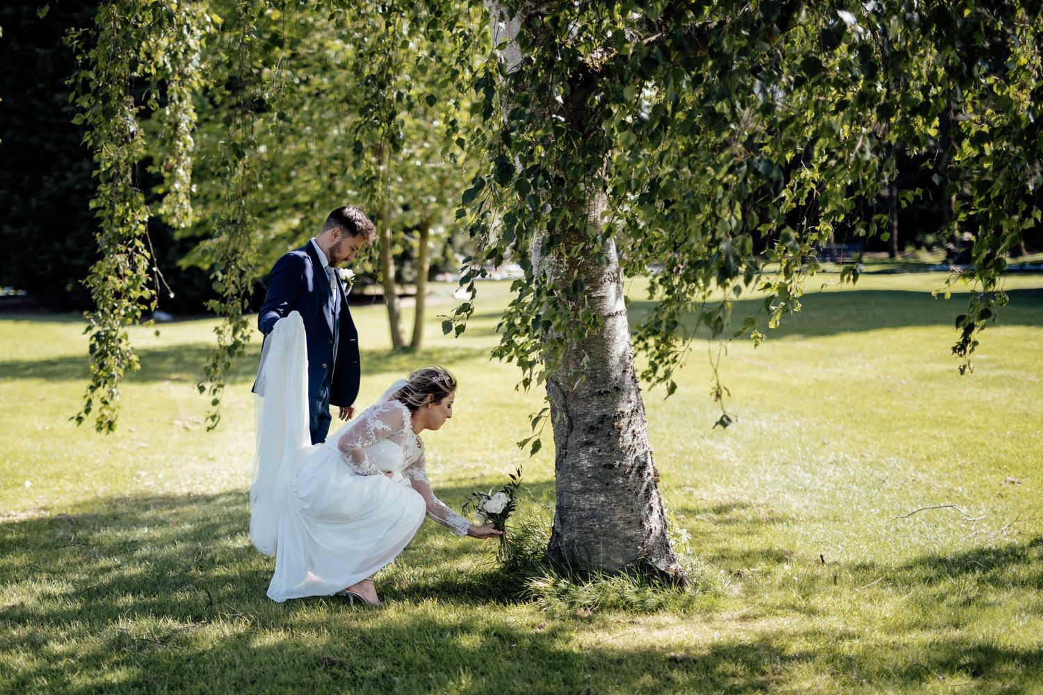 Wedding couple posing playfully under a birch tree in a sunlit garden.