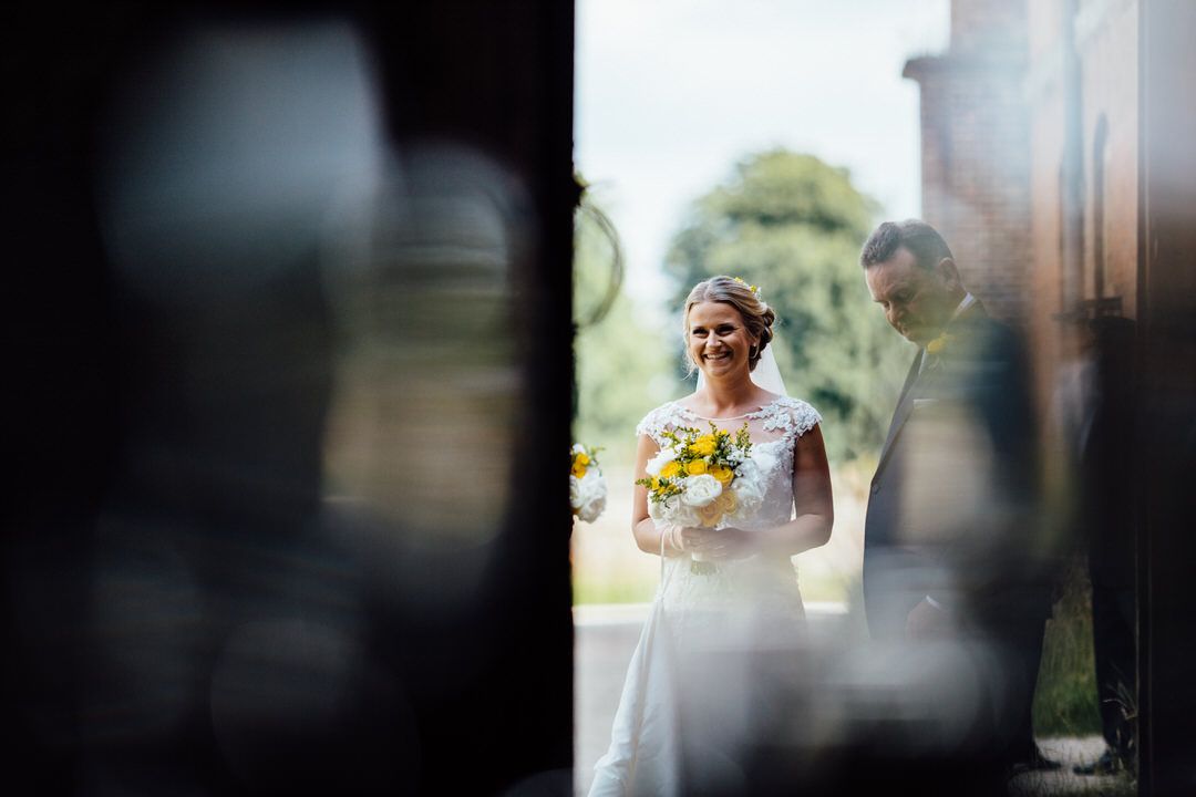 Wedding party members pose together in a garden setting with bright sunlight filtering through trees.