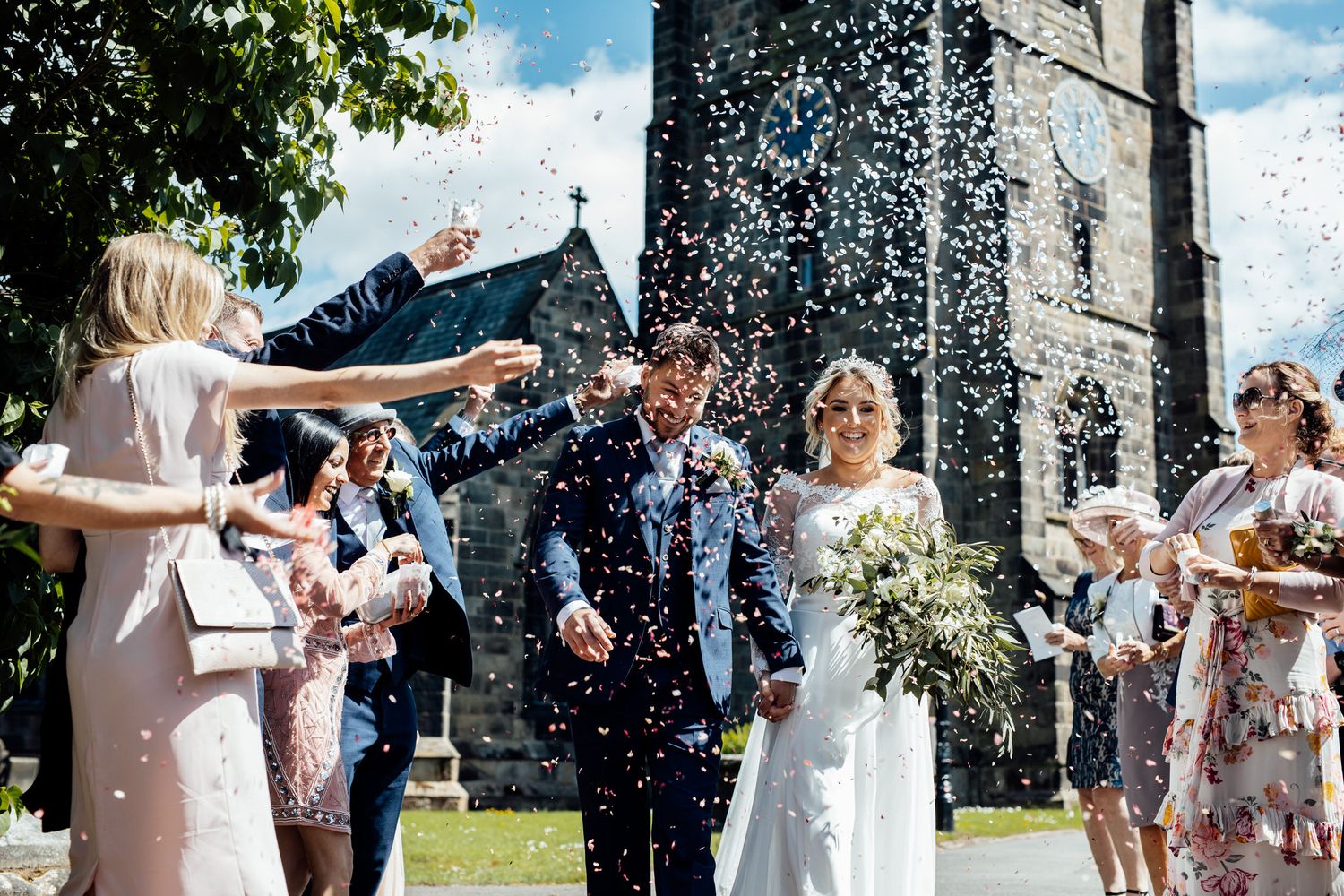 Wedding guests throwing confetti outside a stone church during celebration.