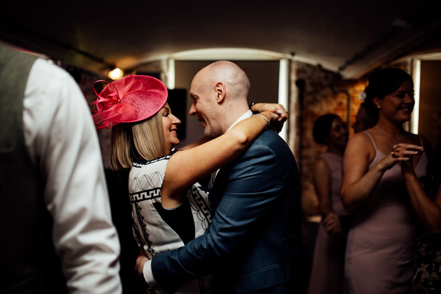 Wedding reception guests dancing in a dimly lit venue with festive atmosphere.