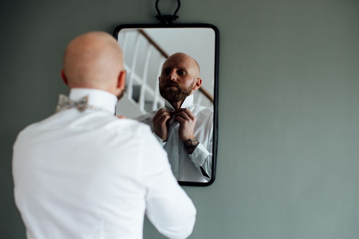A person adjusts their tie while looking in a mirror during wedding preparations.