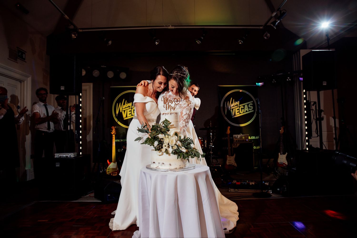 Wedding reception tables with white linens and centerpieces in dimly lit venue.