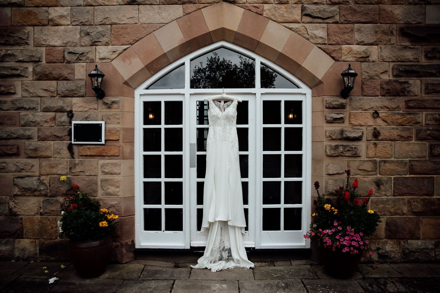 White wedding dress hanging in front of elegant arched French doors with stone facade.