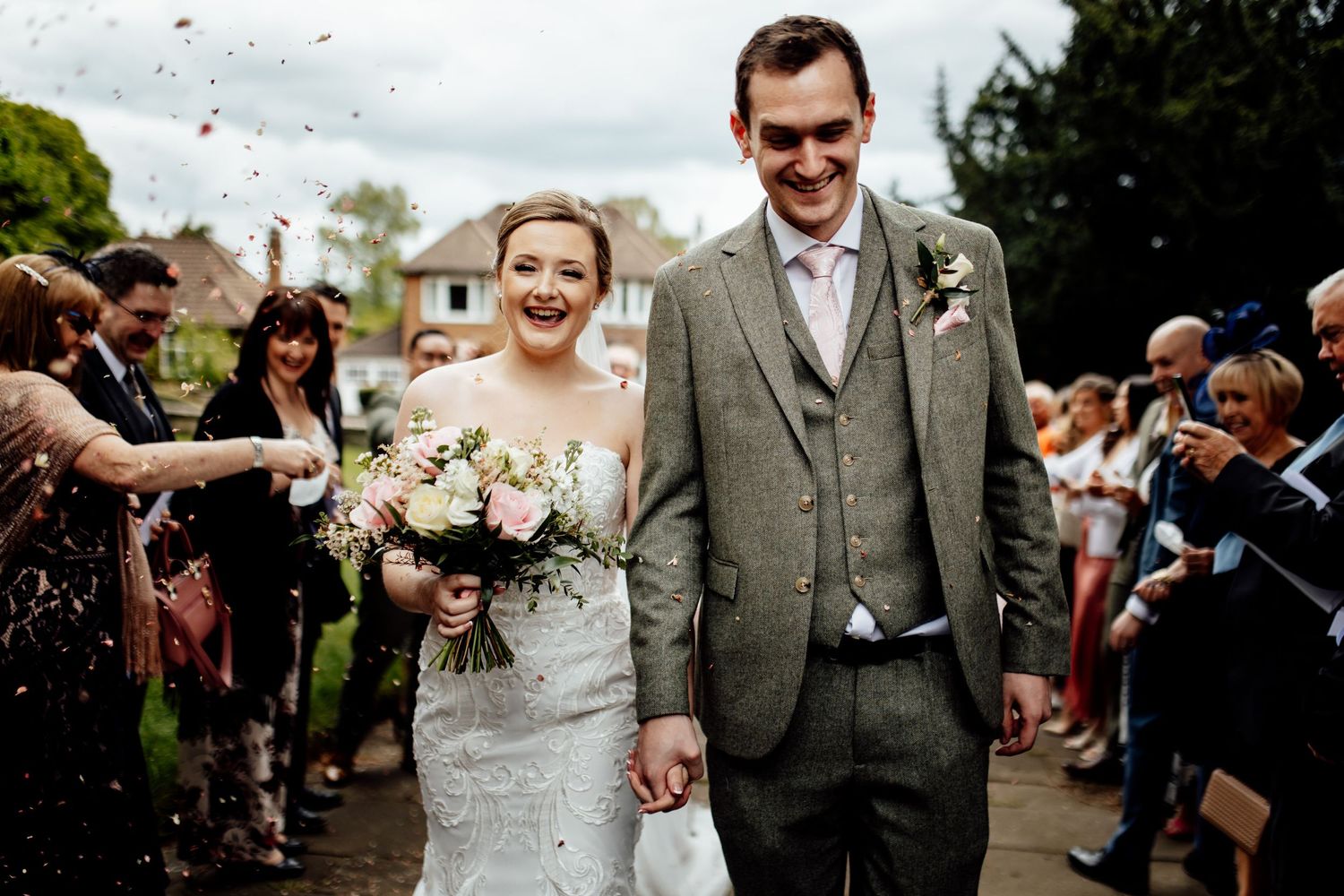 Newlyweds walk through shower of confetti on church path surrounded by guests.